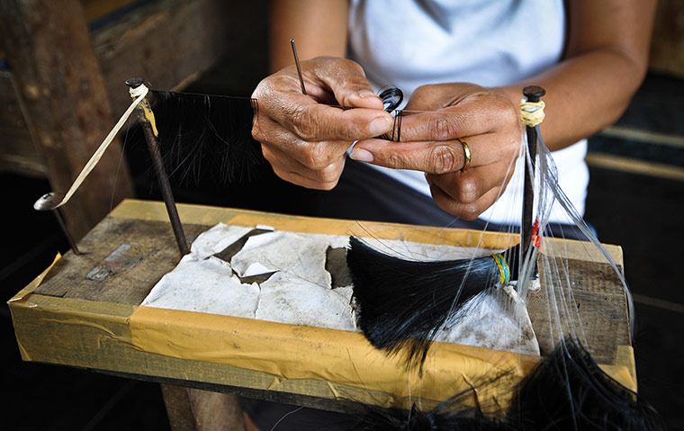Eyelashes: A woman knits strands of hair onto a length of nylon twine