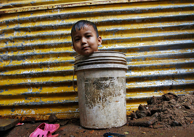 Photo highlights : A boy sits in a bucket while waiting for his mother to fetch water from a n