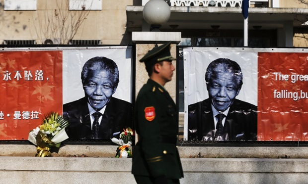 A Chinese security officer walks past images of Nelson Mandela at the Embassy of South Africa in Beijing, China.