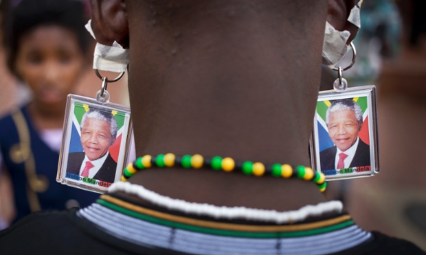 A man wears keyrings showing the face of Mandela taped to his ears to mimic earrings as he and others celebrate his life in Soweto.