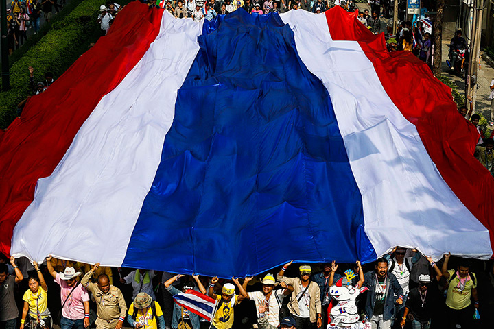 Thailand protests: Anti-government protesters march with a large Thai national flag during a r
