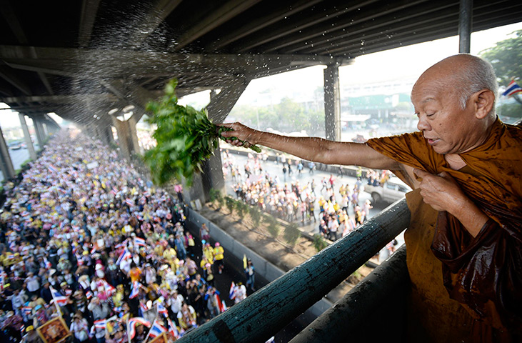 Thailand protests: A monk blesses anti-government protesters as they march under a footbridge