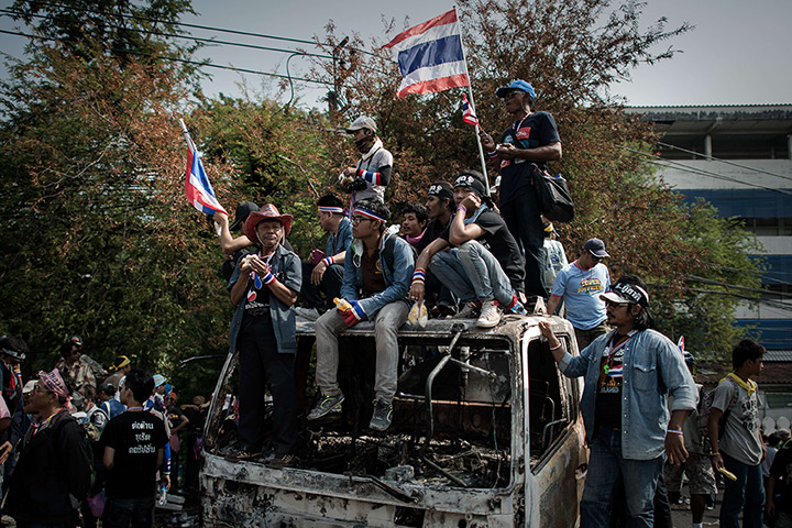 Thailand protests: Demonstrators sit on a burnt police vehicle outside the government building