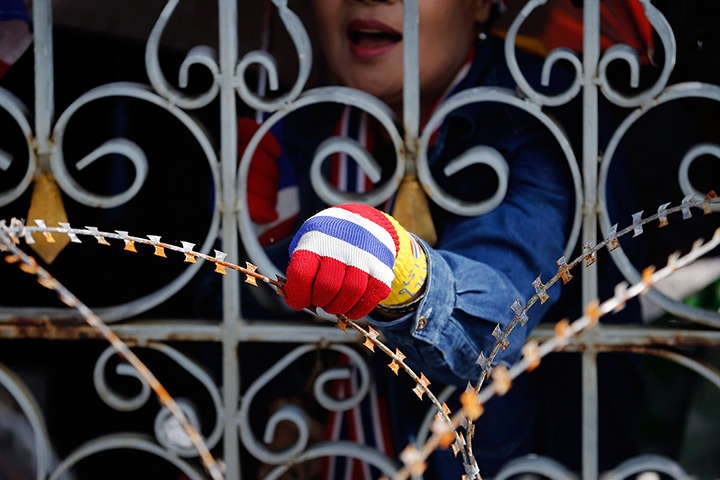 Thailand protests: An anti-government protester holds razor wire from behind a fence as thousa