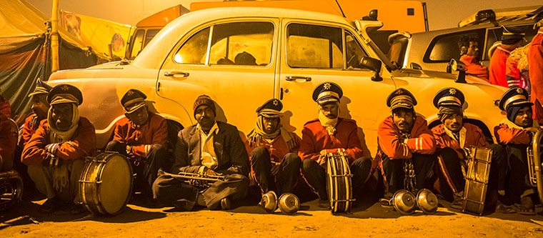 Maha Kumbh : Members of a marching band rest in front of an old Ambassador car