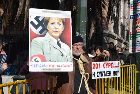 A demonstrator holds up an image of German Chancellor Angela Merkel dressed as a Nazi, while the man holding it has a noose around his neck, during the protest. -