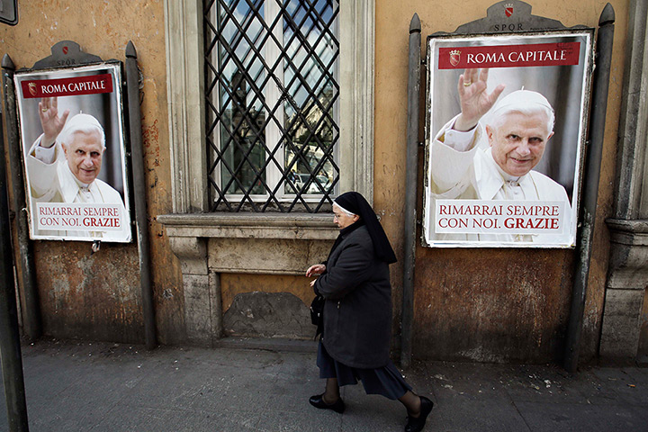 The Pope's last day: A nun walks past posters of Pope Benedict XVI 