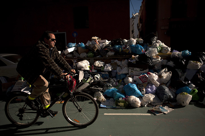 24 hours: Seville, Spain: A man rides past uncollected rubbish