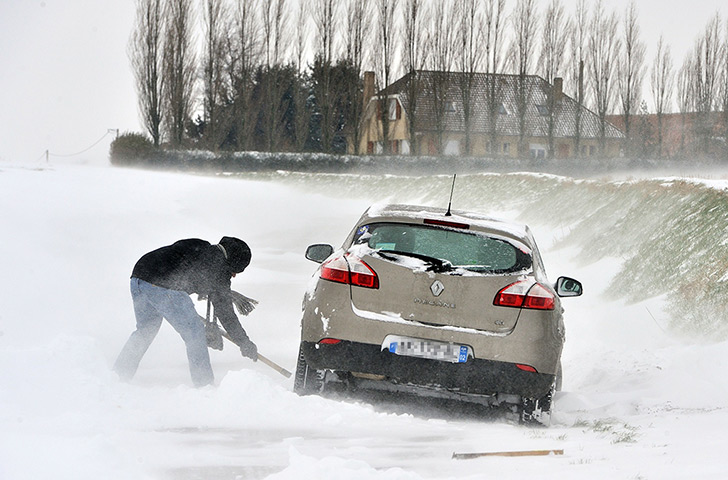 Europe snow: A car driver uses a shovel to remove snow from under his car 