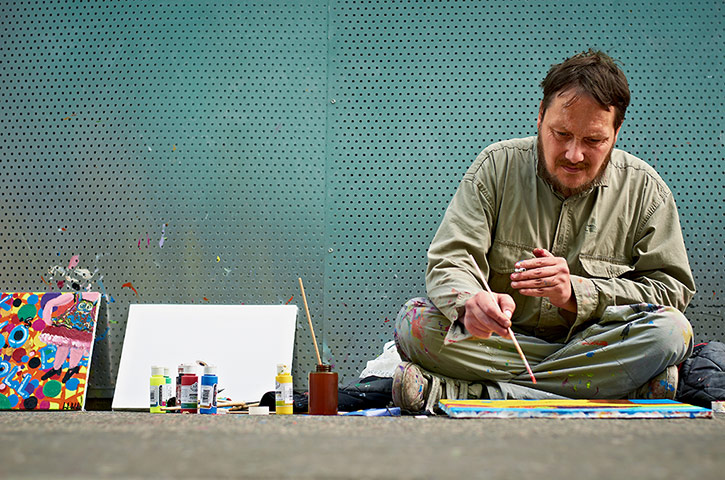 Your pictures - station: man sitting on ground cross-legged painting with a brush