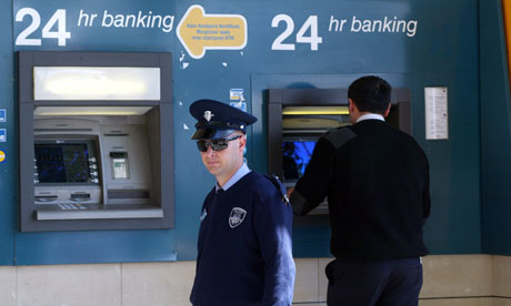 Um policial fica perto de um caixa eletrônico fora de um ramo de Laiki banco em Nicósia, Chipre