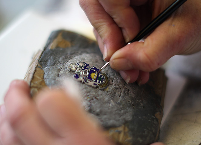 FTA: Christopher Furlong: A craftswoman hand paints enamels on a badge 