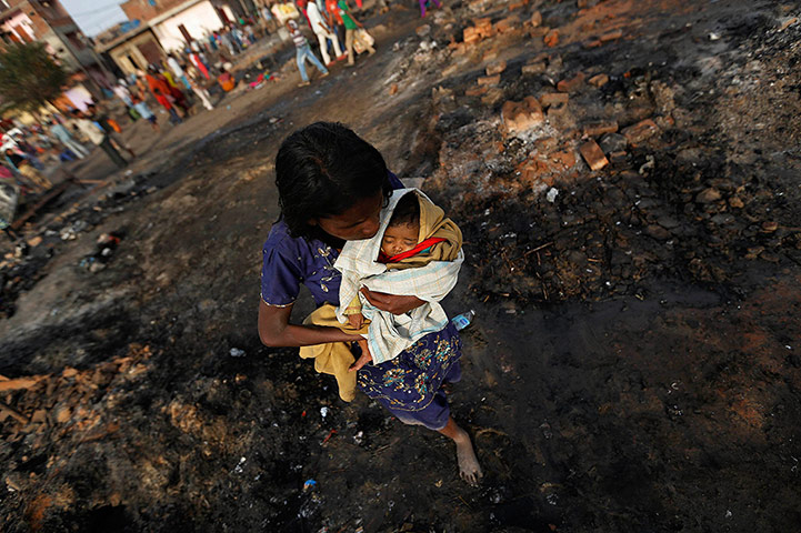 24 Hours: A woman carries her baby through the burnt debris of huts in New Delhi