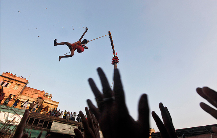 24 hours: Kolkata, India: A Hindu devotee hanging from a rope throws offerings toward