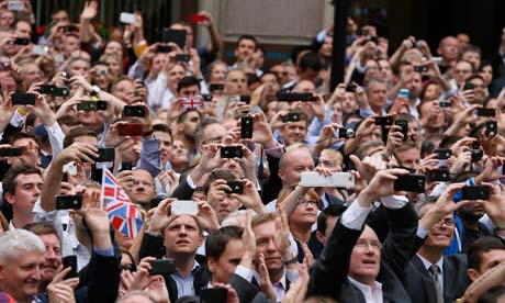 Spectators take pictures with their smartphones as they watch a parade celebrating Britain's athlete