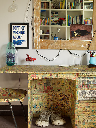 homes - lou rota: table covered in comic strip paper with shelving above