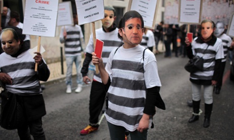 A demonstrator wearing a mask of Portuguese prime minister Pedro Passos Coelho, carries a sign with the words 