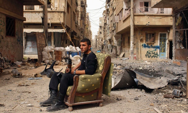 A member of the Free Syrian Army holds his weapon as he sits on a sofa in the middle of a street in Deir al-Zor.