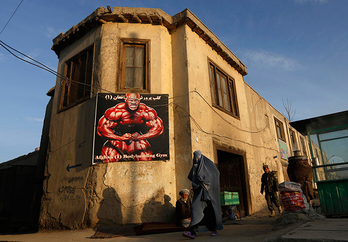 24 hours: Kabul, Afghanistan: A woman in a burqa walks past a poster for a gym 