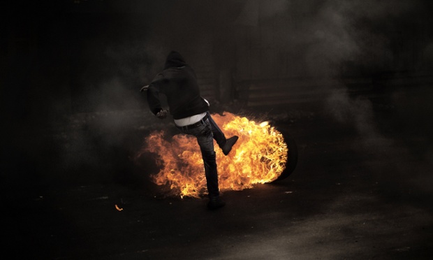 A Palestinian demonstrator kicks a flaming tyre.