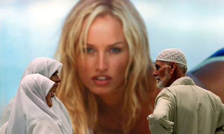 TURKISH MOSLEMS CHAT IN FRONT OF AN ADVERTISEMENT AT ISTANBUL AIRPORT