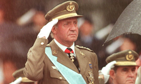 Rey Juan Carlos de España saluda durante un desfile militar en la lluvia