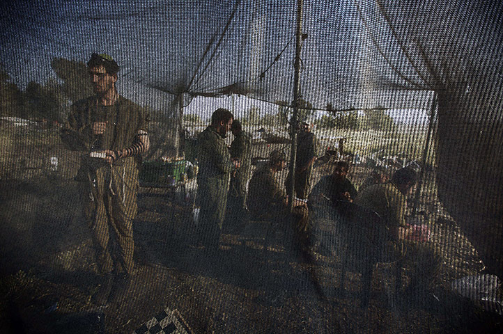 20 Photos: An Israeli soldier prays inside a net tent pitched close to Merkava tanks