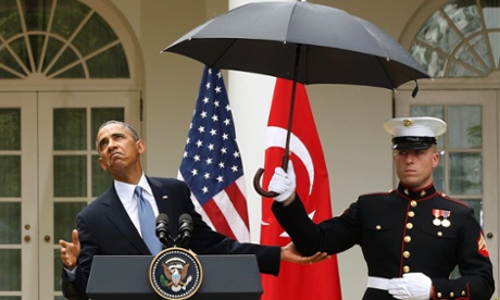 Barack Obama checks to see if he still needs the umbrella held by a US marine.