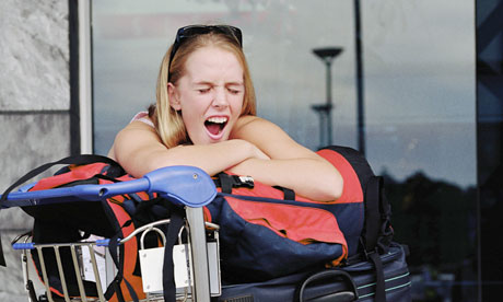 Jet lag. Young woman leaning on luggage on trolley, yawning