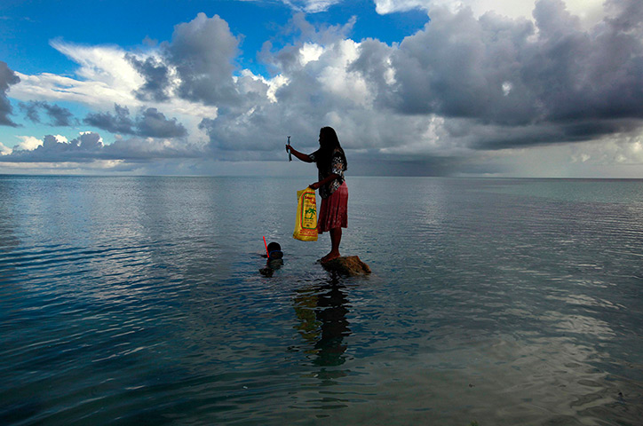 Kiribati, Pacific island: Binata Pinata stands on top of a rock holding a fish her husband Kaibakia j