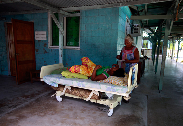 Kiribati, Pacific island: A woman prepares to feed a patient on a bed, placed outside due to lack of 