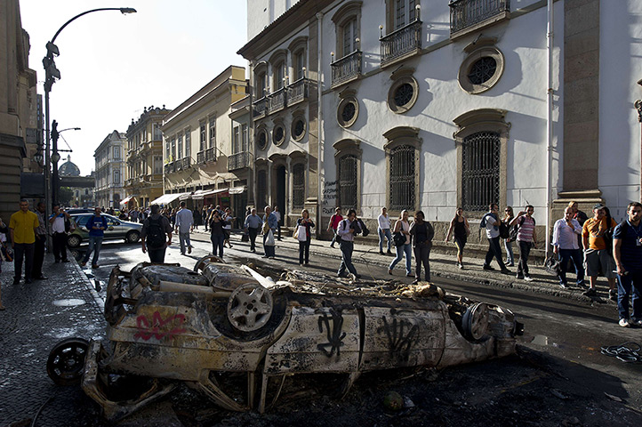 Brazil protests continue: People pass by a car burnt out car in downtown Rio de Janeiro,