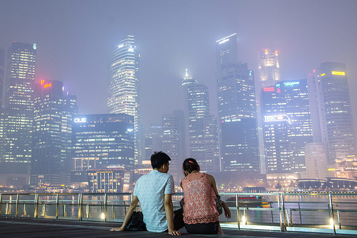 Singapore smog: A couple relaxes on the boardwalk along Marina Bay, with the skyline shroud