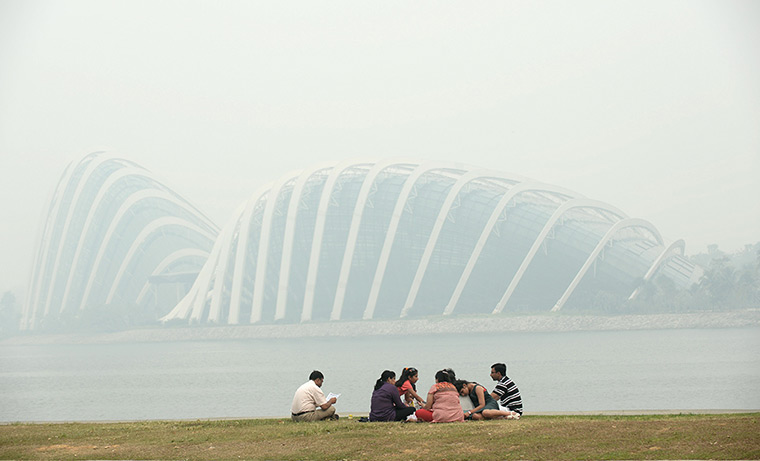 Singapore smog: A group of people sit along the bay as the Garden by the Bay's domes are sh