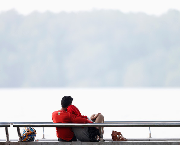 Singapore smog: A couple sits in a park near a river against a sky blanketed by light haze 