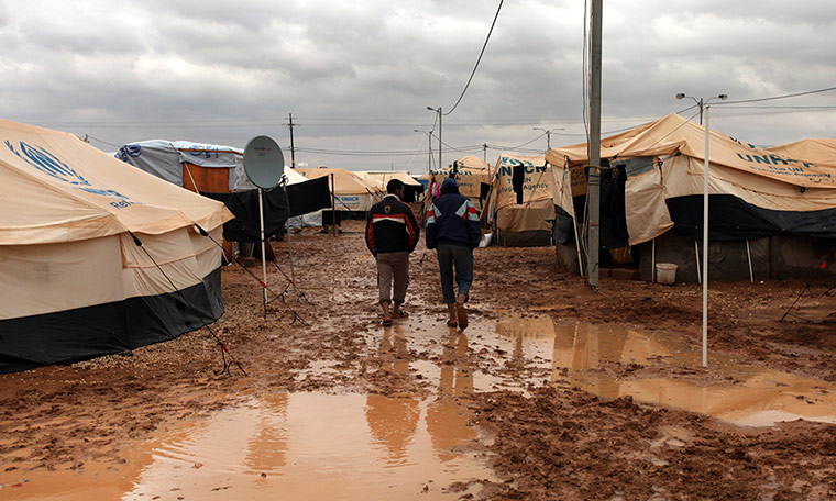 Syrian refugees: Two men walk among tents, surrounded by water and mud, at Zaatari camp 