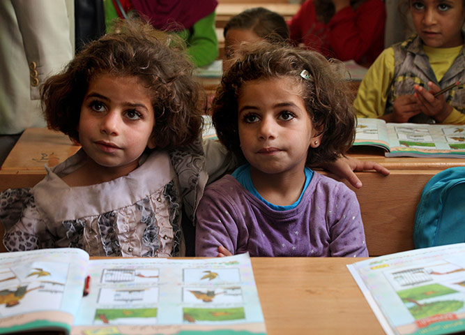 Syrian refugees: Twin sisters sit at their desks in a refugee camp, Jordan