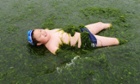 A boy plays on an algae-covered seaside in Qingdao, Shandong province