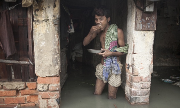 A man eats his lunch in front of his house amid flood waters.