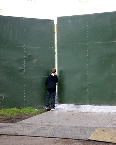 Big Picture - Peeking: boy looking through gap in green hoarding