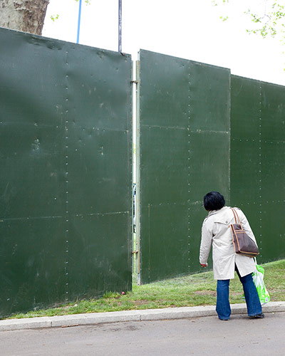 Big Picture - Peeking: woman looking through gap in green hoarding