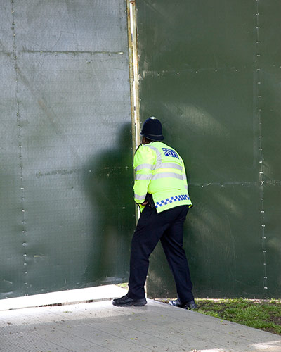 Big Picture - Peeking: Policeman looking through gap in green hoarding