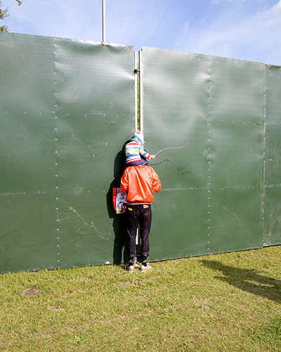 Big Picture - Peeking: child on adult's shoulders looking through gap in hoarding