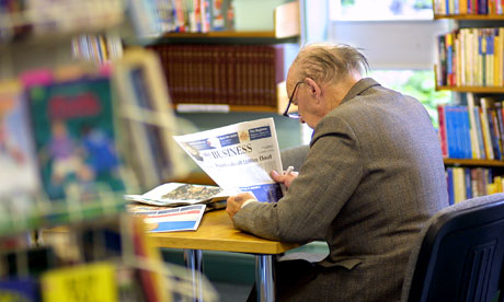 Elderly man reading a newspaper in a library