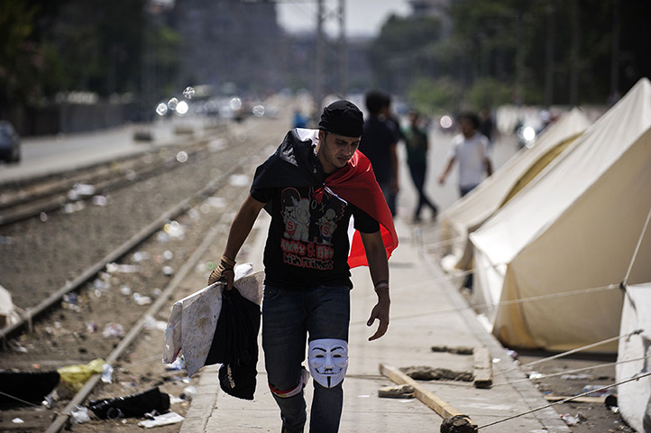 Egypt update: An Egyptian protester with a Guy Fawkes mask on his knee walks past tents s