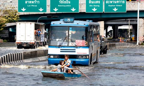 Residents row a boat in front of a bus along a flooded street in Bangkok