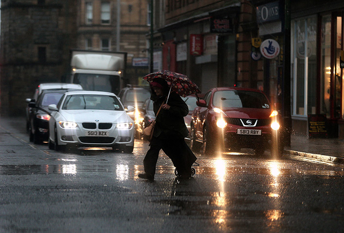 Stormy weather: A woman crosses the road during heavy rain in Glasgow, Scotland