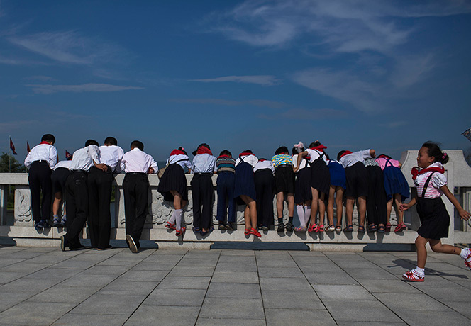 North Korea 60th: North Korean school children lean over a foot bridge to see carp swimming i