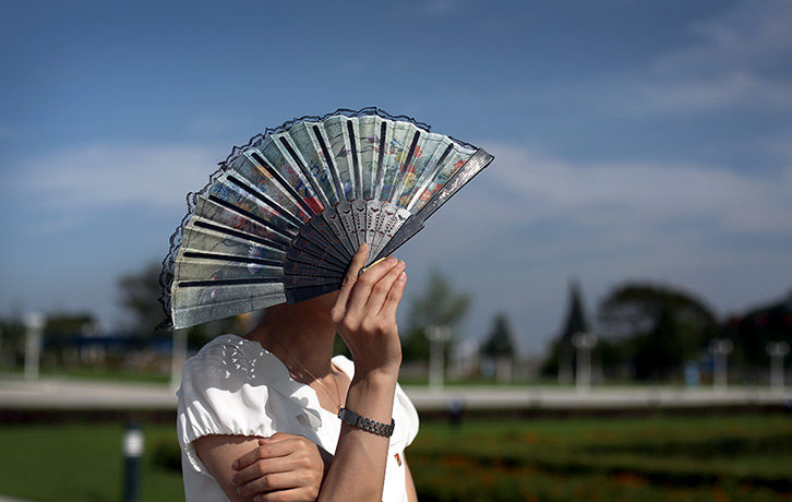 North Korea 60th: A guide shields her face from the sun while touring the park surrounding Ku