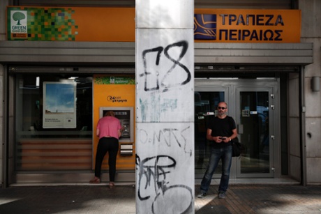 A woman makes a transaction at an ATM of a Piraeus Bank branch as a man waits for his turn in Athens July 25, 2013.